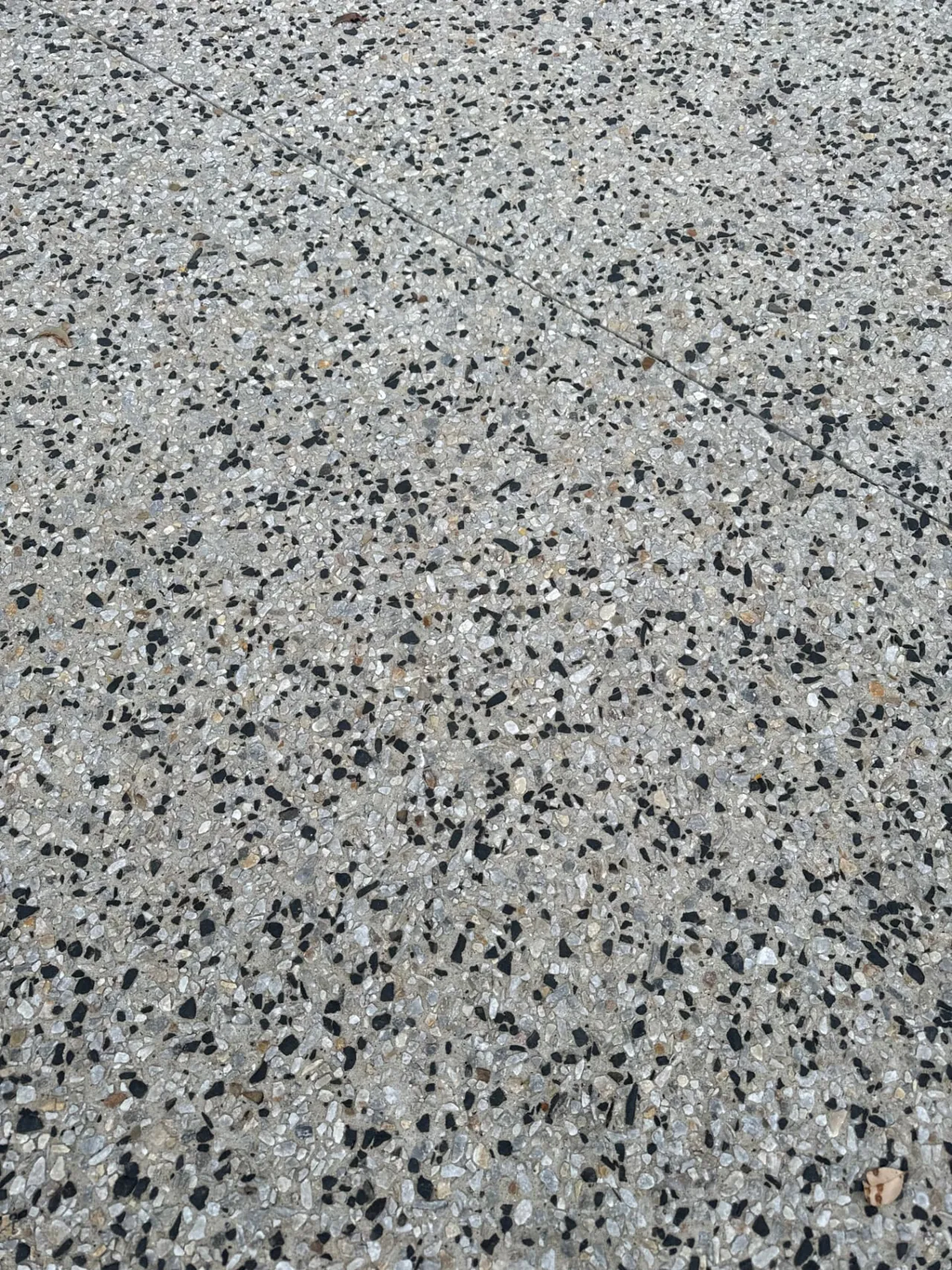 Close up of a black and white exposed aggregate concrete surface with a control joint
